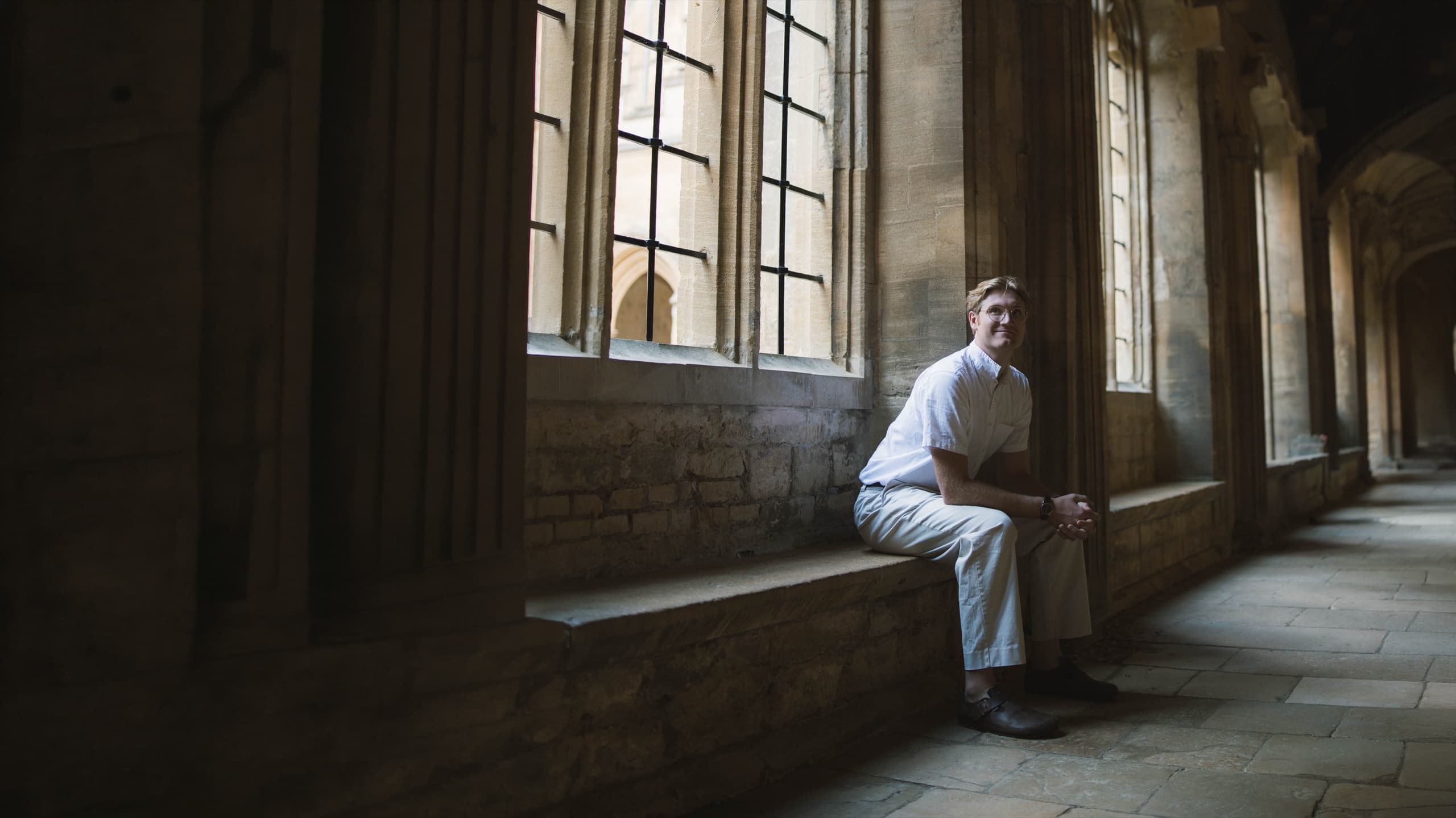 Enoch seated on a stone window ledge in a cloister
